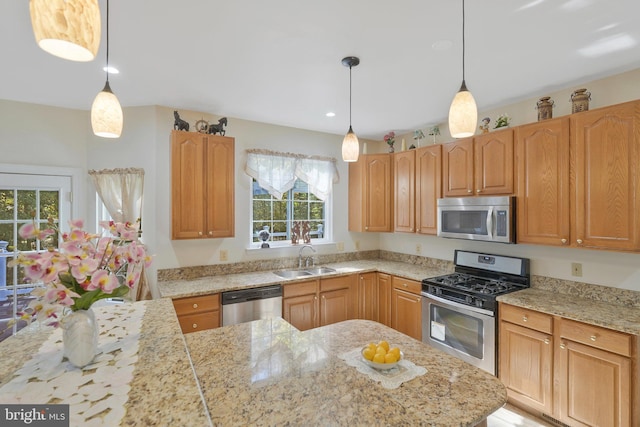 kitchen featuring decorative light fixtures, stainless steel appliances, light stone counters, and sink