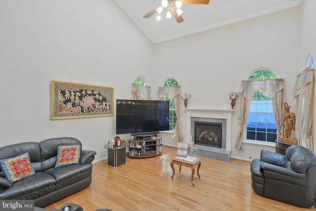 living room with ceiling fan, high vaulted ceiling, crown molding, wood-type flooring, and a tiled fireplace