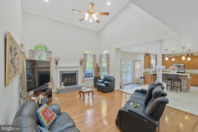 living room with a high ceiling, crown molding, light hardwood / wood-style flooring, ceiling fan, and a fireplace