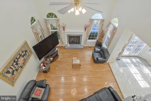 living room featuring ceiling fan, wood-type flooring, a high ceiling, and a tiled fireplace