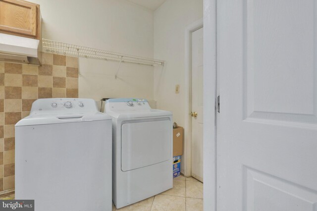 laundry area featuring light tile patterned floors, tile walls, and washing machine and clothes dryer