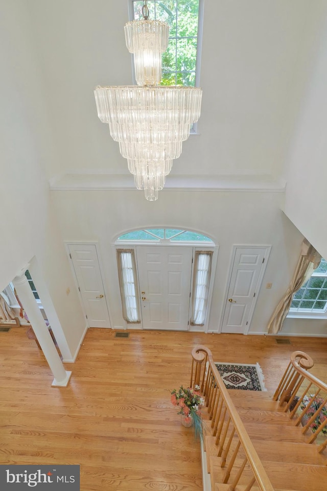 entrance foyer featuring plenty of natural light, wood-type flooring, a towering ceiling, and a chandelier