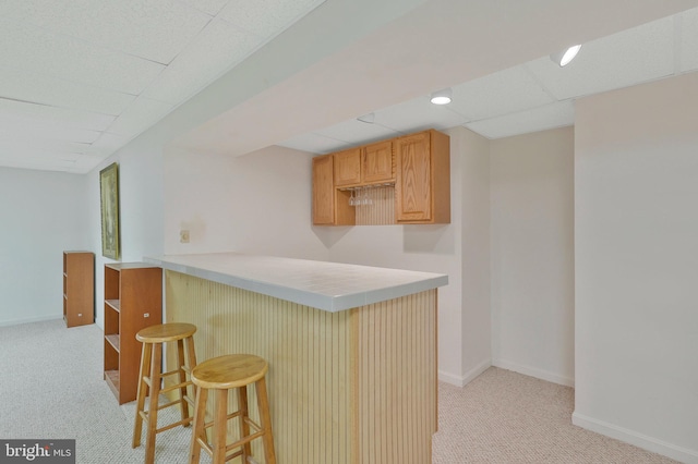 kitchen featuring a paneled ceiling, a kitchen breakfast bar, light colored carpet, and kitchen peninsula