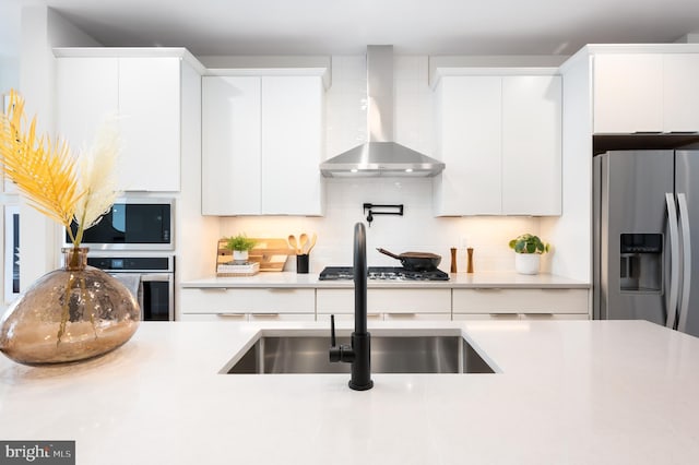 kitchen featuring white cabinets, appliances with stainless steel finishes, decorative backsplash, and wall chimney range hood