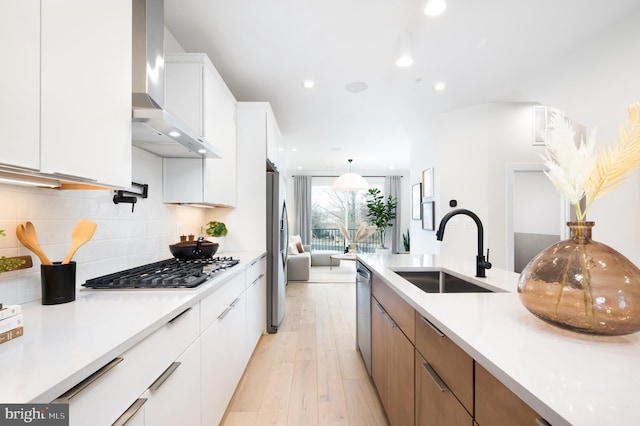 kitchen with white cabinets, sink, light hardwood / wood-style flooring, wall chimney exhaust hood, and stainless steel appliances