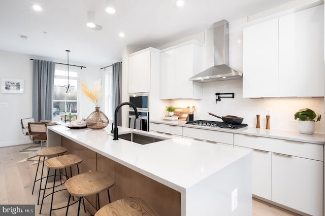 kitchen with white cabinets, wall chimney range hood, and an island with sink