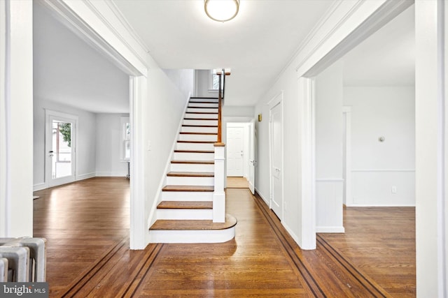 stairs with radiator heating unit, crown molding, and hardwood / wood-style floors