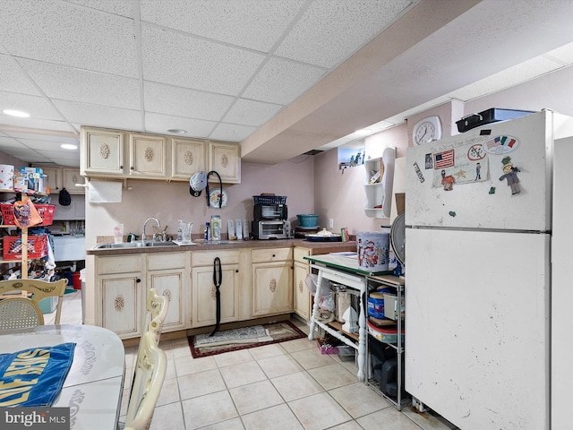 kitchen with a drop ceiling, sink, light tile patterned flooring, and white fridge