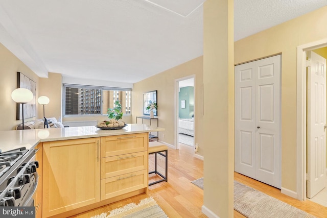 kitchen with kitchen peninsula, light hardwood / wood-style floors, a textured ceiling, light brown cabinetry, and stainless steel range with gas stovetop