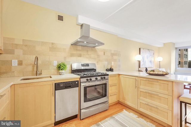 kitchen with kitchen peninsula, tasteful backsplash, stainless steel appliances, sink, and wall chimney range hood