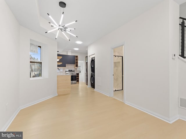 unfurnished living room with light hardwood / wood-style flooring, stacked washer / drying machine, and a notable chandelier