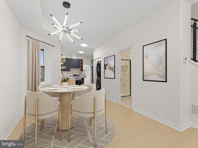 dining space with an inviting chandelier, stacked washer and dryer, and light hardwood / wood-style flooring