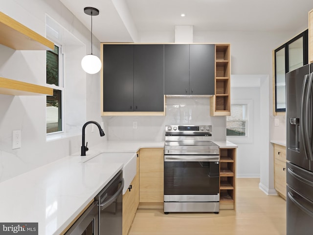 kitchen featuring light stone countertops, sink, decorative light fixtures, appliances with stainless steel finishes, and light wood-type flooring