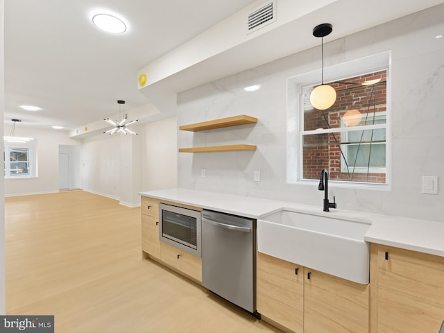 kitchen with appliances with stainless steel finishes, light brown cabinetry, sink, decorative light fixtures, and light hardwood / wood-style flooring