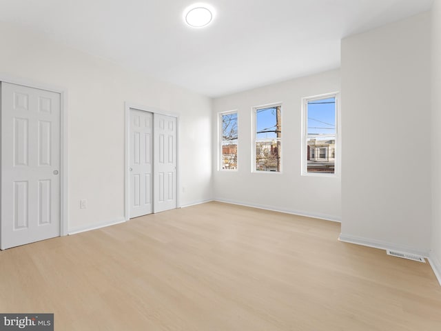 unfurnished bedroom featuring light wood-type flooring and multiple closets