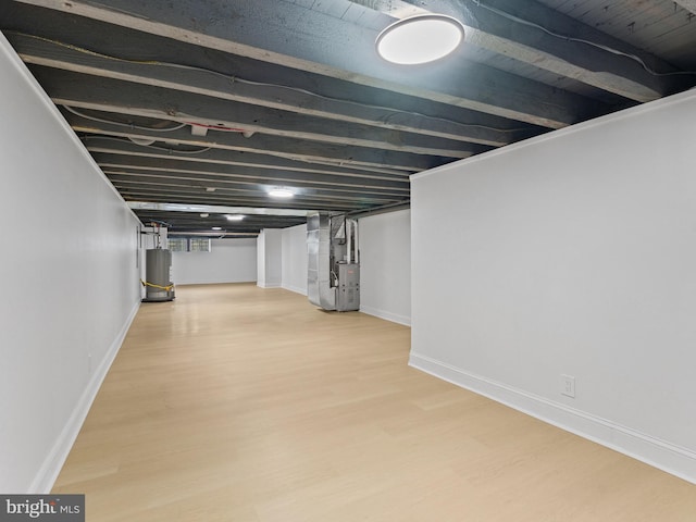 basement featuring water heater, light hardwood / wood-style flooring, and heating unit