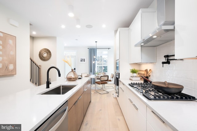 kitchen with stainless steel appliances, sink, wall chimney range hood, decorative light fixtures, and white cabinets