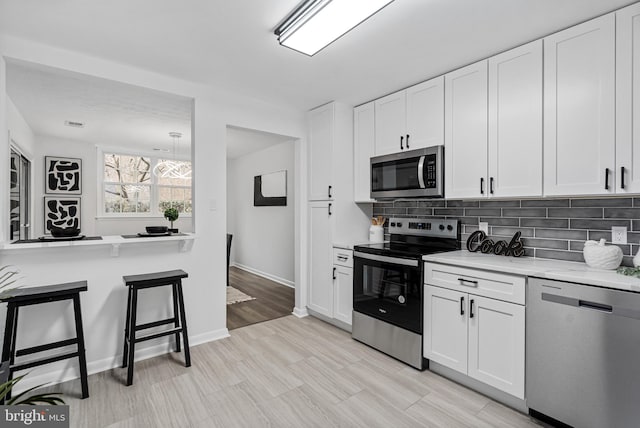 kitchen featuring appliances with stainless steel finishes, white cabinetry, backsplash, a kitchen breakfast bar, and light stone countertops