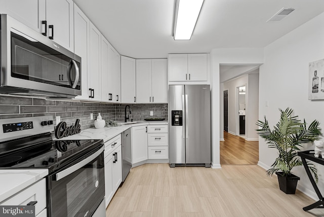 kitchen featuring sink, appliances with stainless steel finishes, white cabinetry, backsplash, and light stone countertops