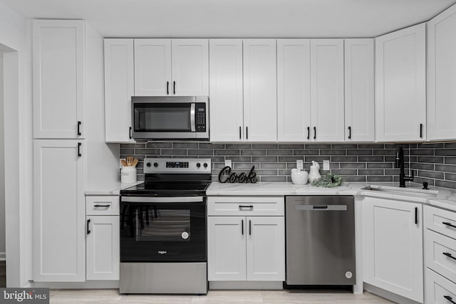 kitchen with white cabinetry, appliances with stainless steel finishes, light stone countertops, and sink