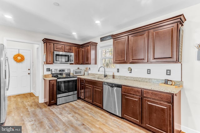 kitchen with light stone countertops, light wood-type flooring, stainless steel appliances, and sink