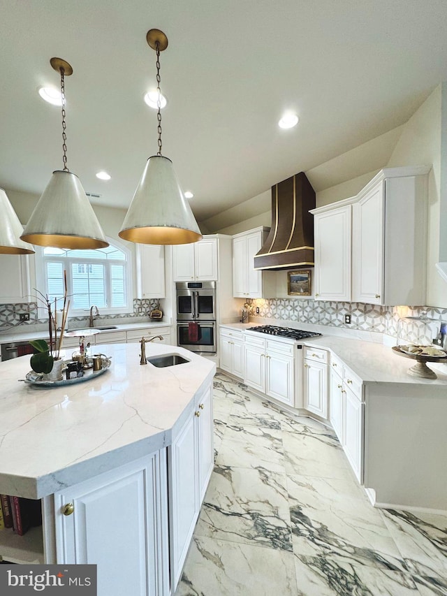 kitchen featuring a center island with sink, custom exhaust hood, white cabinetry, and hanging light fixtures