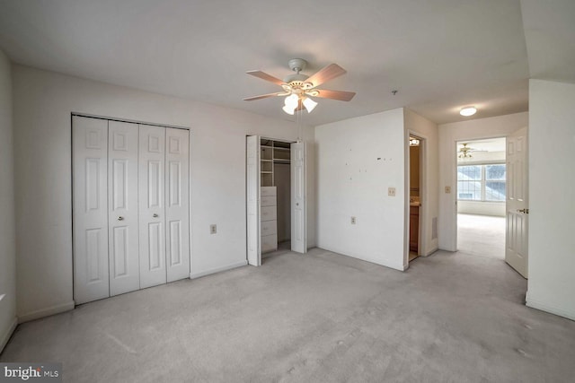 unfurnished bedroom with light carpet, multiple closets, and ceiling fan