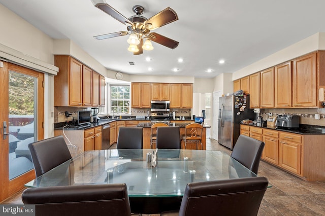 kitchen featuring sink, ceiling fan, a kitchen island with sink, stainless steel appliances, and tasteful backsplash