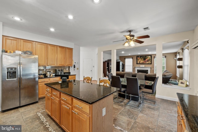 kitchen featuring a kitchen island, dark stone counters, ceiling fan, and stainless steel refrigerator with ice dispenser