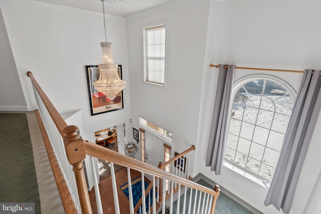 staircase featuring crown molding, a healthy amount of sunlight, carpet floors, and a notable chandelier