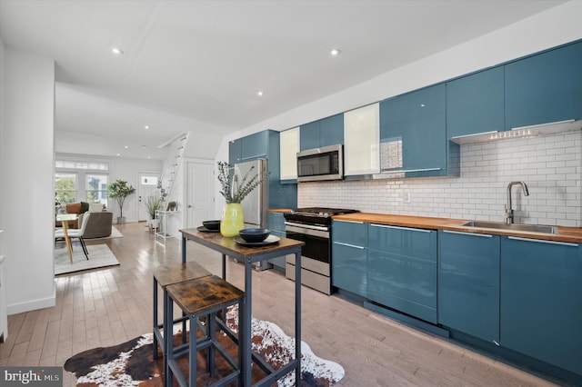 kitchen featuring backsplash, sink, blue cabinetry, butcher block counters, and stainless steel appliances