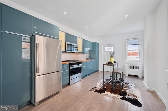 kitchen with decorative backsplash, stainless steel appliances, blue cabinetry, light hardwood / wood-style flooring, and radiator heating unit