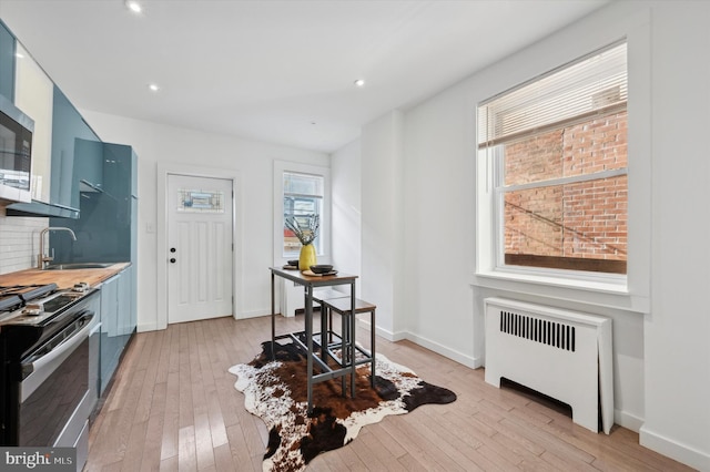 kitchen featuring blue cabinets, light hardwood / wood-style flooring, decorative backsplash, radiator heating unit, and stainless steel appliances