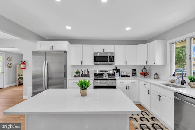 kitchen featuring appliances with stainless steel finishes, light wood-type flooring, a kitchen island, sink, and white cabinetry