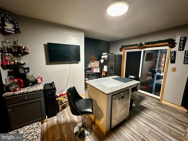 kitchen featuring light stone countertops, light hardwood / wood-style floors, black fridge, and a breakfast bar area