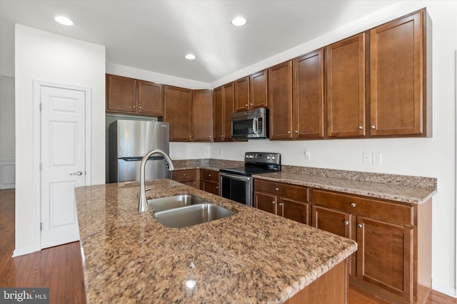 kitchen with a kitchen island with sink, sink, dark wood-type flooring, and appliances with stainless steel finishes