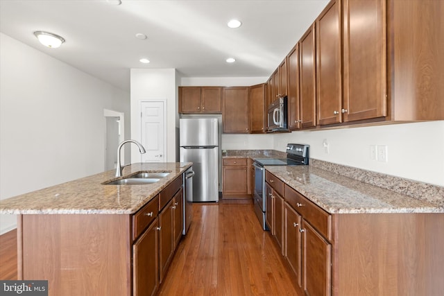 kitchen with sink, stainless steel appliances, light stone counters, a kitchen island with sink, and light wood-type flooring