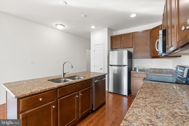 kitchen with a kitchen island with sink, dark wood-type flooring, sink, appliances with stainless steel finishes, and light stone counters