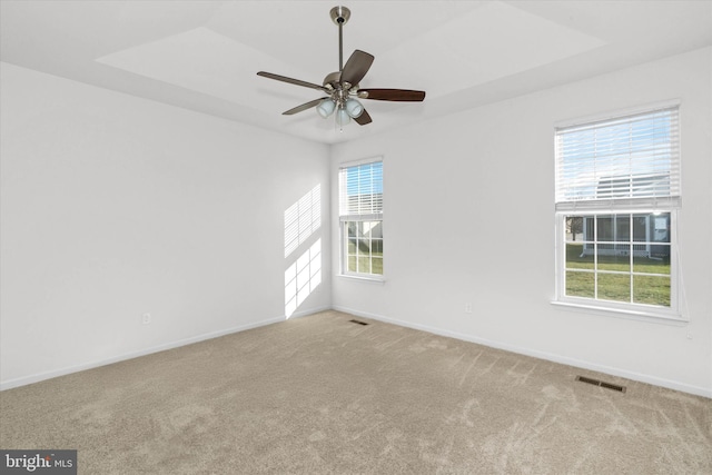 empty room with a tray ceiling, light carpet, and ceiling fan