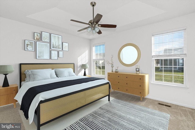 bedroom with ceiling fan, light carpet, and a tray ceiling