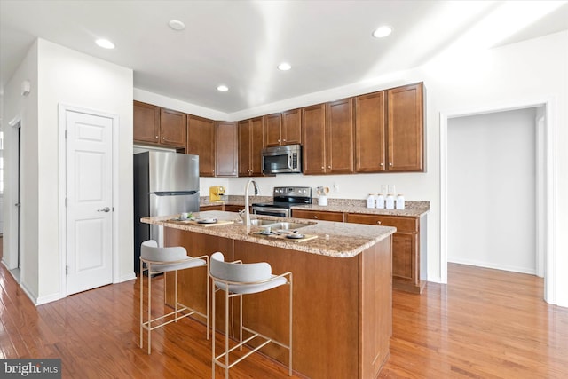 kitchen featuring appliances with stainless steel finishes, a center island with sink, light hardwood / wood-style flooring, and a kitchen breakfast bar