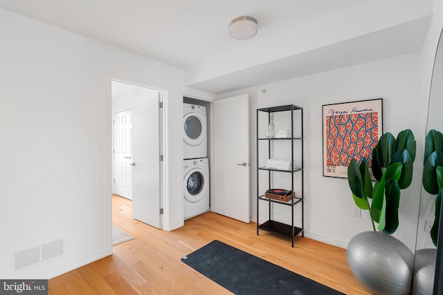 clothes washing area with stacked washer and dryer and wood-type flooring