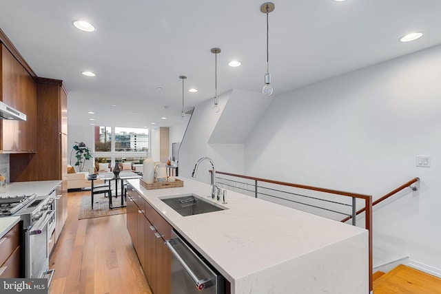 kitchen with a center island with sink, sink, light hardwood / wood-style flooring, decorative light fixtures, and stainless steel appliances