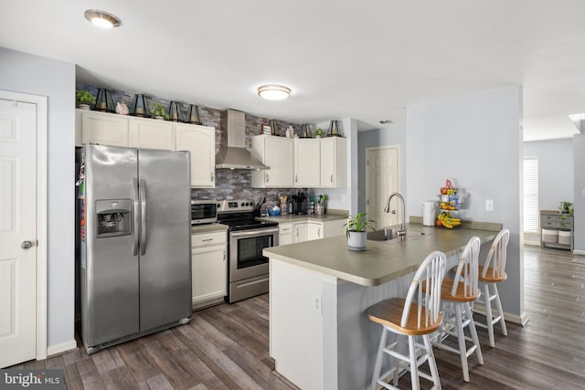 kitchen with kitchen peninsula, wall chimney exhaust hood, stainless steel appliances, sink, and white cabinets