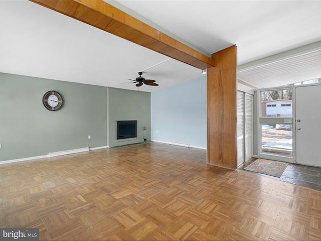 unfurnished living room with ceiling fan, a large fireplace, light parquet floors, and beamed ceiling