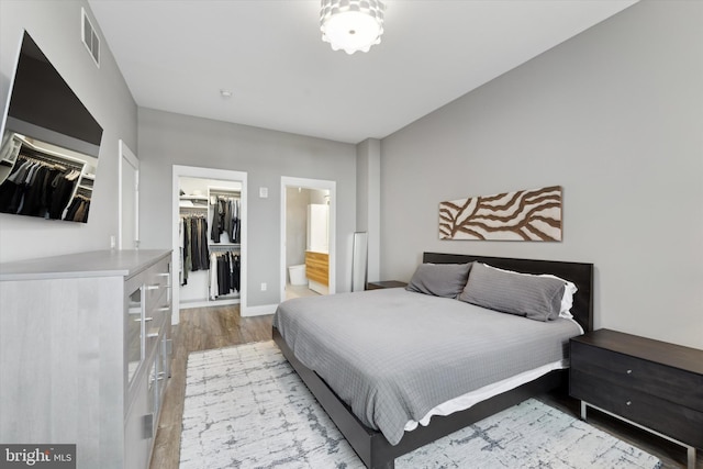 bedroom with ensuite bath, light wood-type flooring, a spacious closet, and a closet