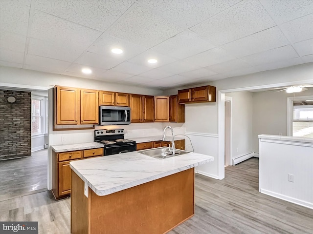 kitchen featuring sink, stainless steel appliances, a baseboard heating unit, hardwood / wood-style floors, and an island with sink