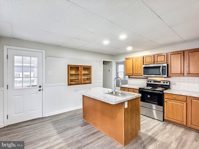 kitchen with sink, a drop ceiling, light hardwood / wood-style floors, a center island with sink, and appliances with stainless steel finishes