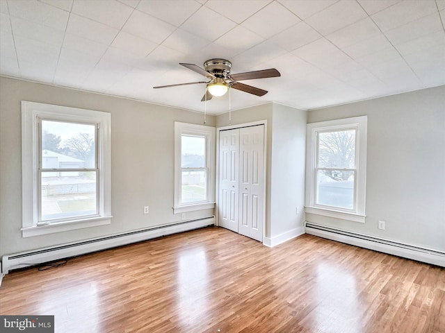 unfurnished bedroom with multiple windows, ceiling fan, and a baseboard heating unit