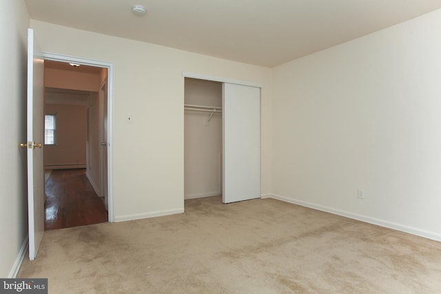 unfurnished bedroom featuring a baseboard heating unit, light carpet, and a closet